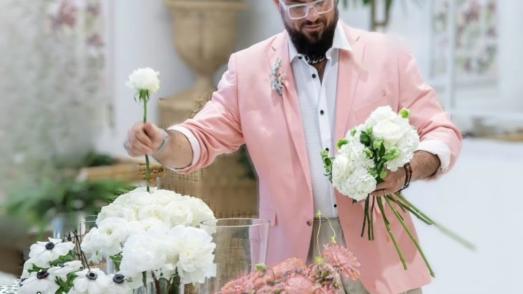 Michael Paris hand-selecting stems and composing a bouquet in the studio, surrounded by fresh floral arrangements.